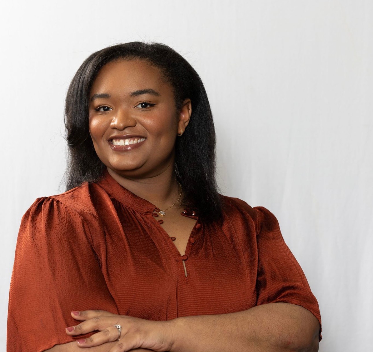 Portrait of Alayna Bouie smiling, in a rust-colored blouse against a soft white backdrop